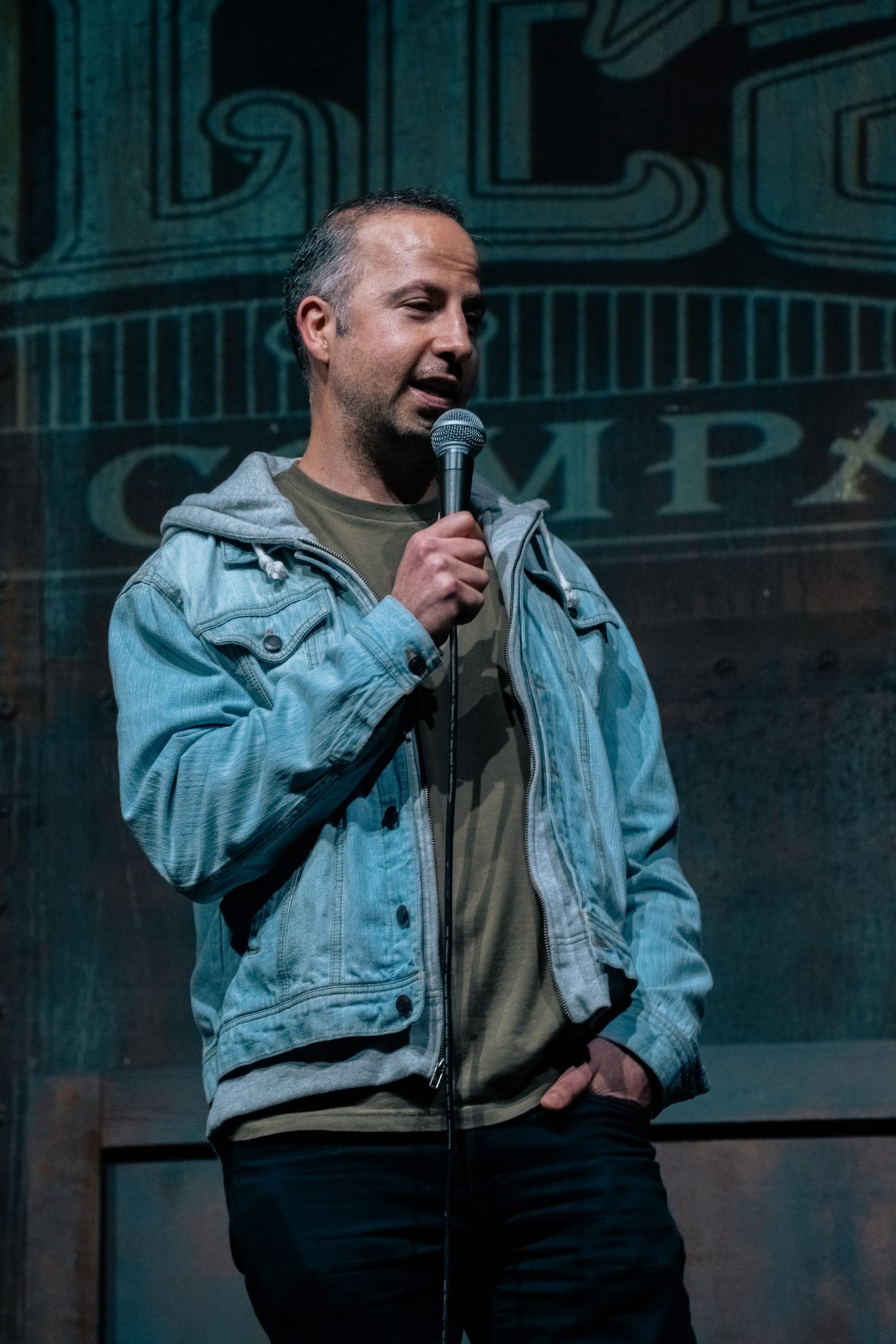 Hal Sadi performing stand-up comedy in a denim jacket